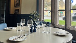 A round dining table with a vase of greenery, wine glasses, and cutlery. - The Swan Inn (Moreton-in-Marsh)