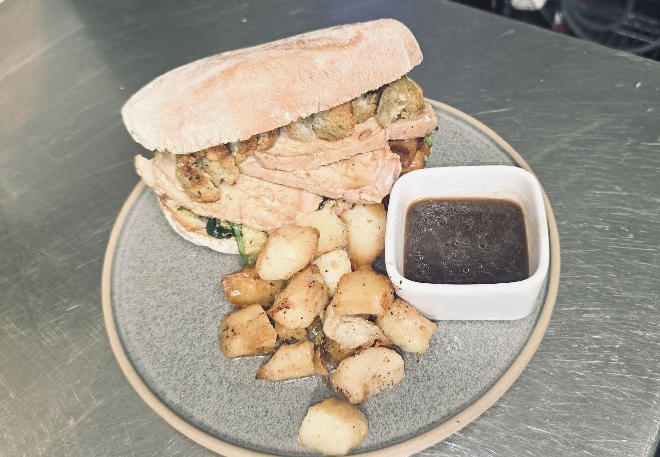 A sandwich with a side of fries and a small container of sauce on a round plate.