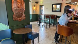 A bar area with stools, a counter, and a wall-mounted sign. - The Swan Inn (Moreton-in-Marsh)