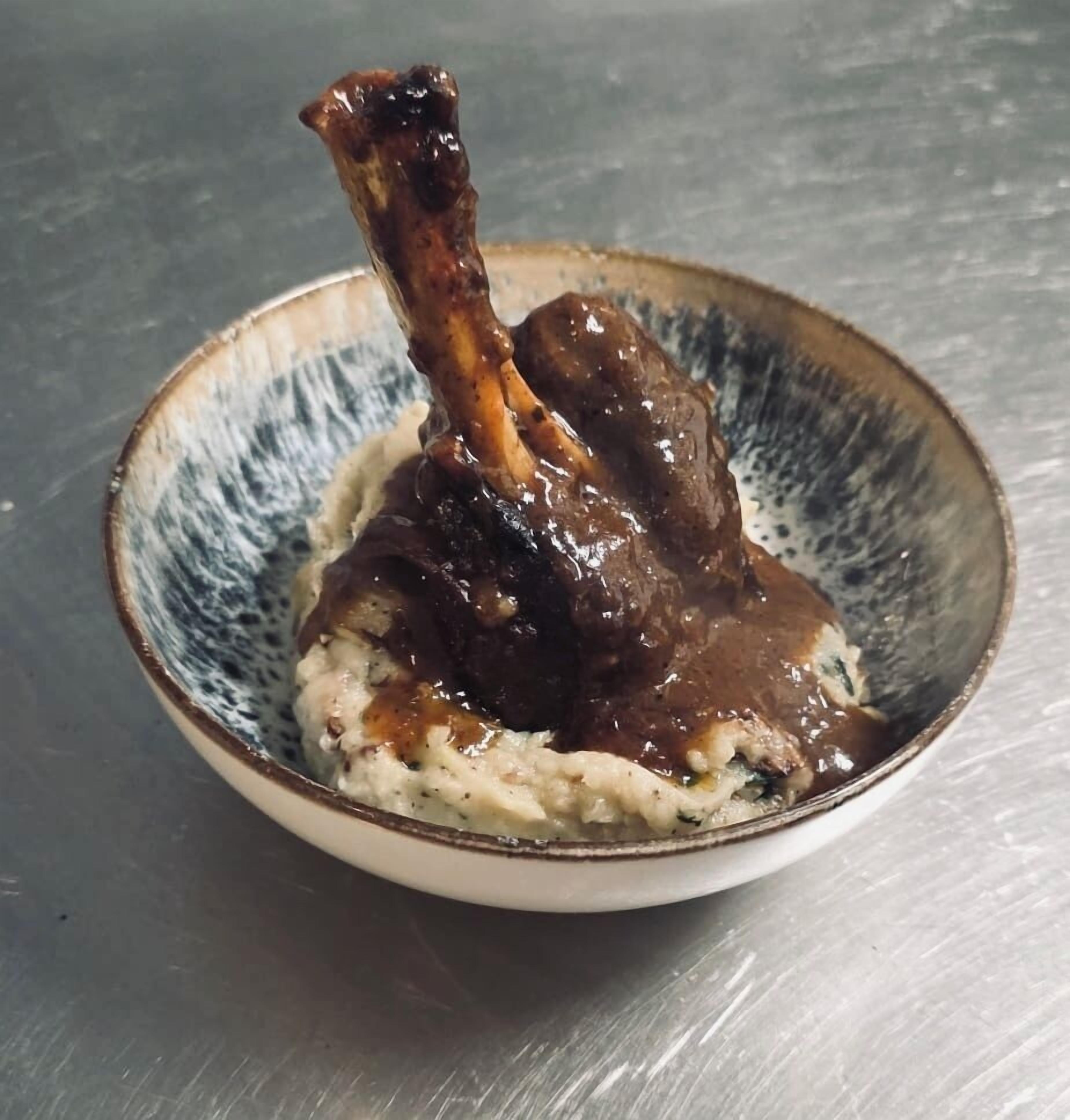 A bowl of food with a bone and sauce, placed on a textured surface.