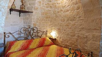 A stone-walled room with a bed, a shelf with decorative items, and a wall-mounted light fixture.