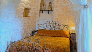 A room with a stone wall, a bed with a metal frame, and a shelf with decorative items.