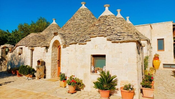 A stone building with conical roofs and a central door, surrounded by potted plants.