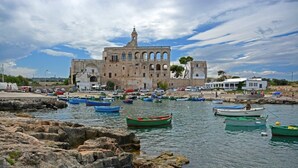 A coastal town with a historic building featuring arches and a bell tower, surrounded by calm waters with small boats.