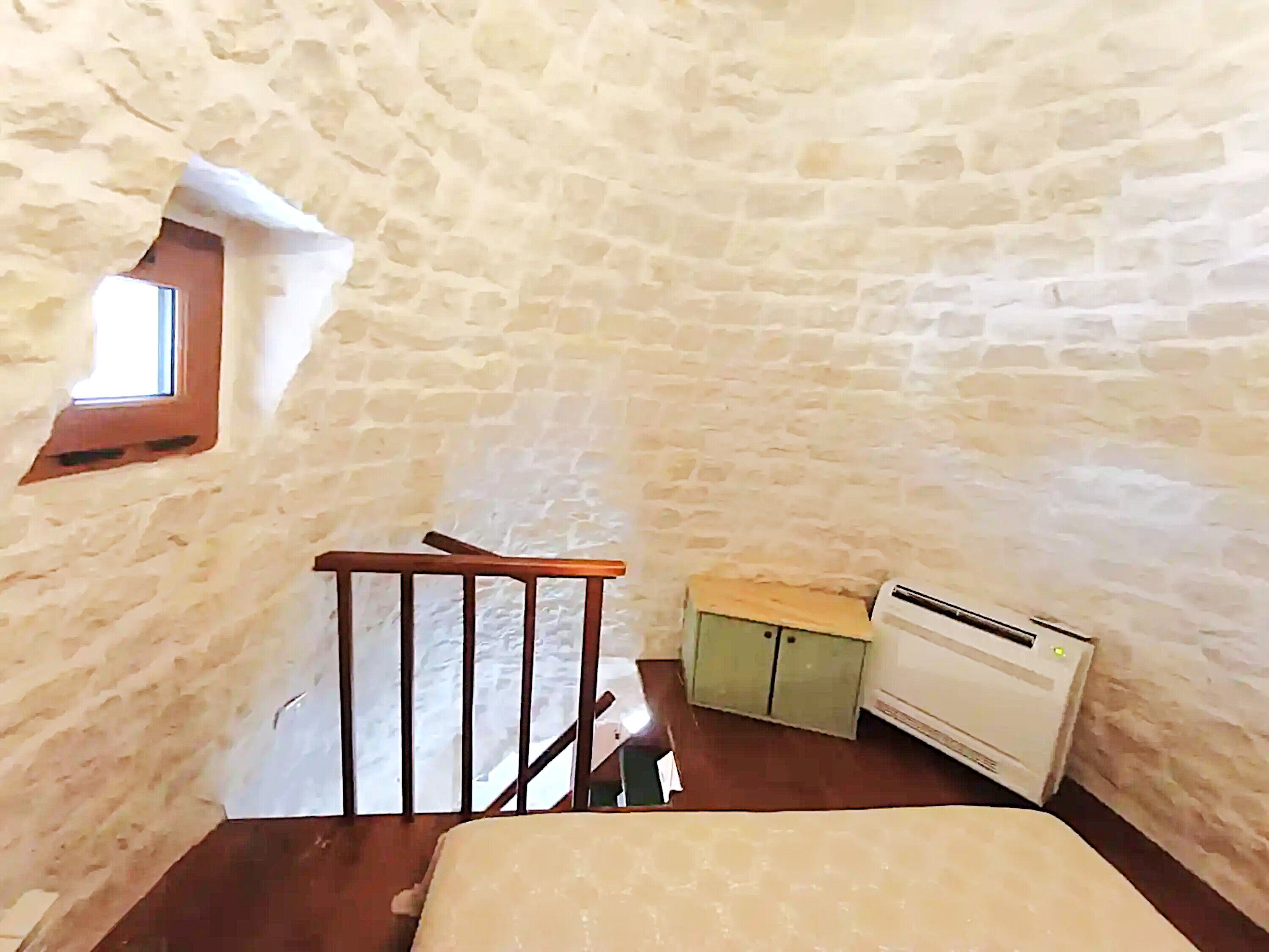 Une pièce avec un plafond en pente, un escalier en bois, un radiateur et une petite fenêtre.