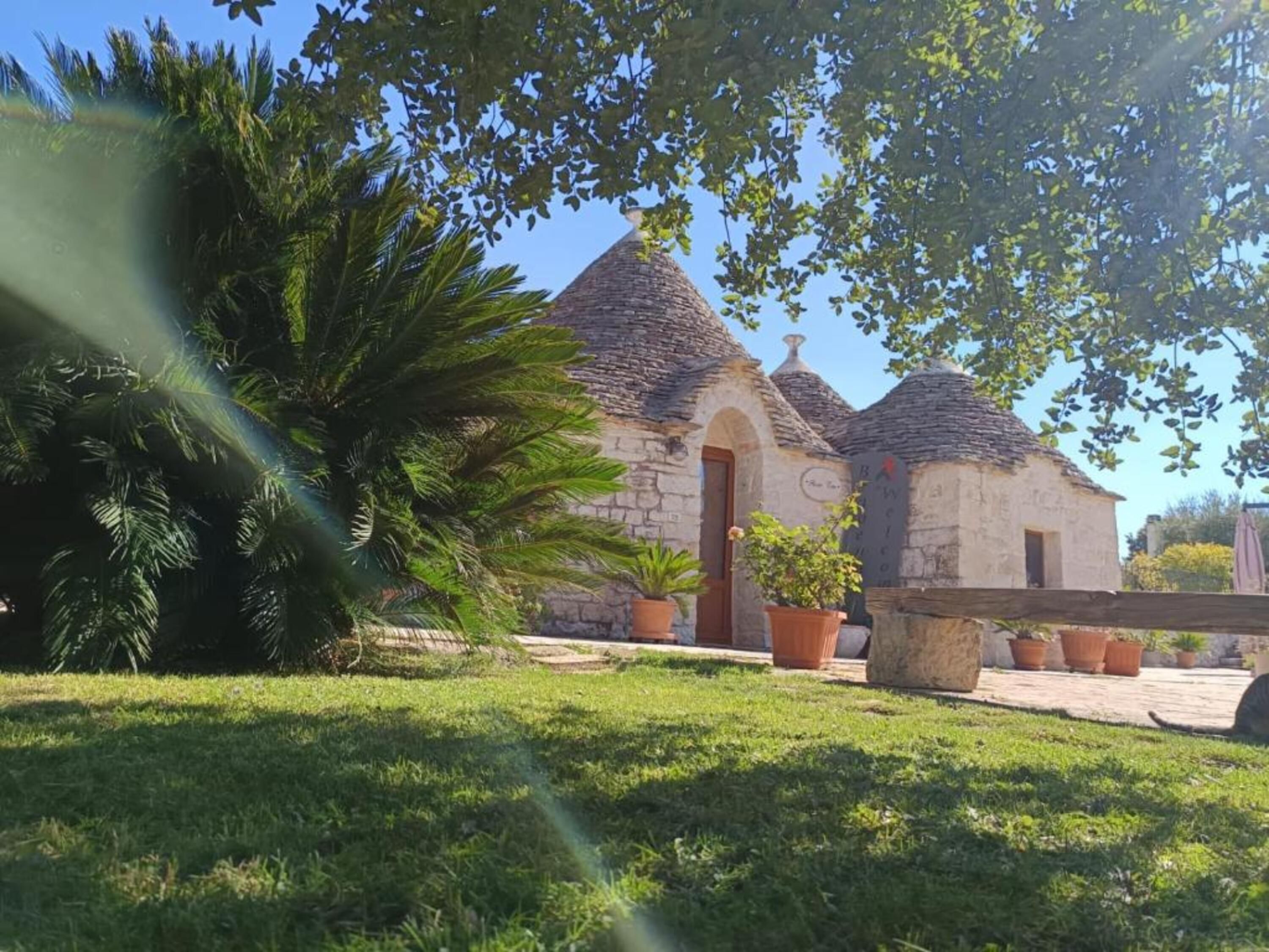 A stone building with a pitched roof, surrounded by grass and potted plants.