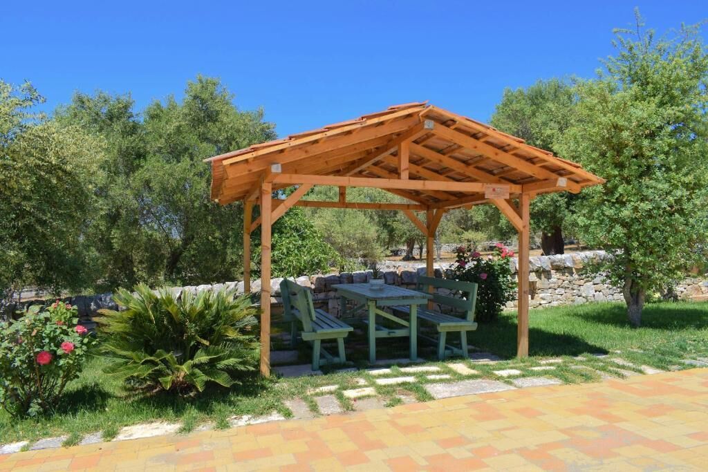 Uma pérgula de madeira com uma mesa e cadeiras em um jardim.