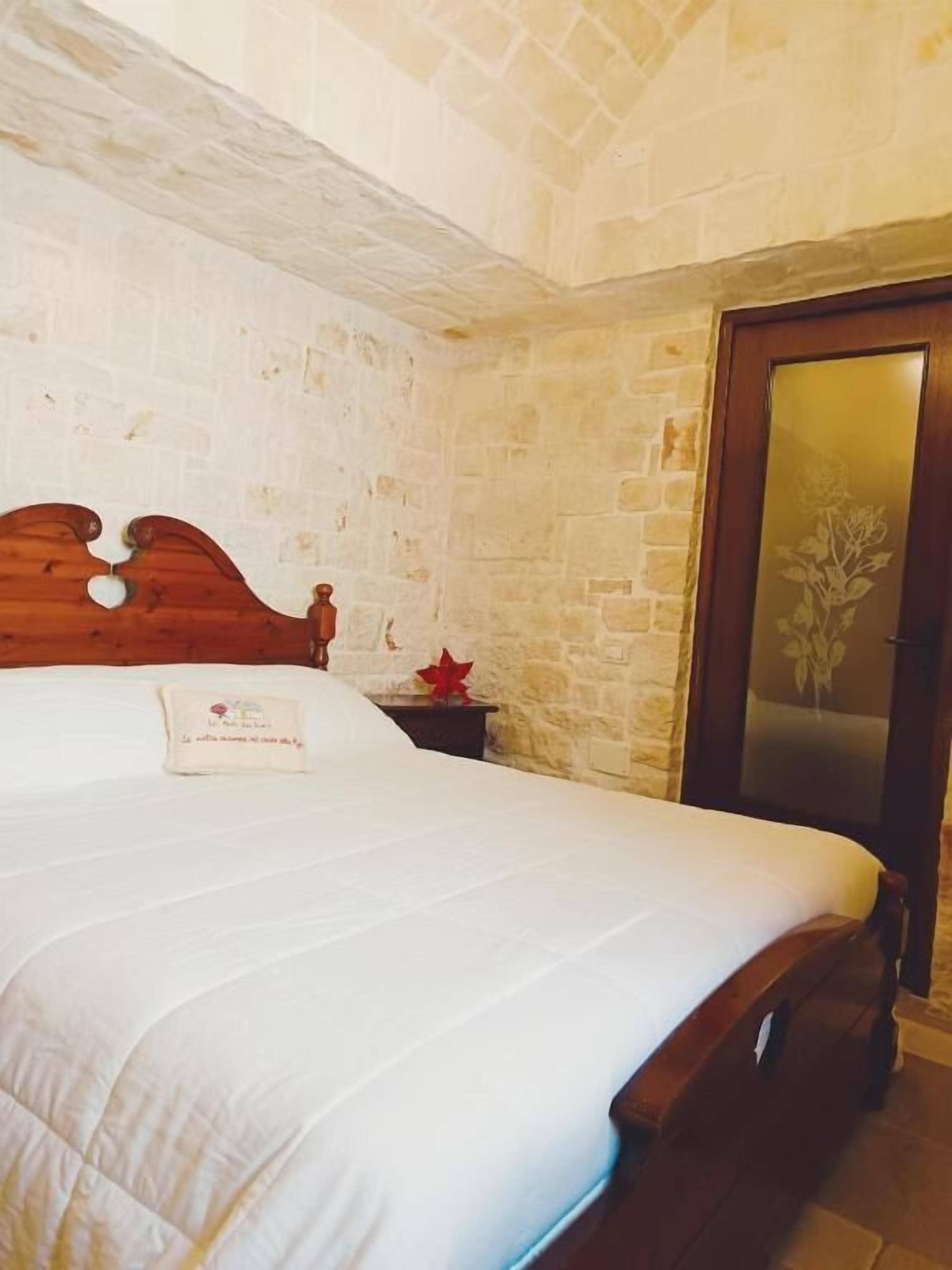 A bedroom with a wooden bed, white bedding, a stone wall, and a door with a floral design.