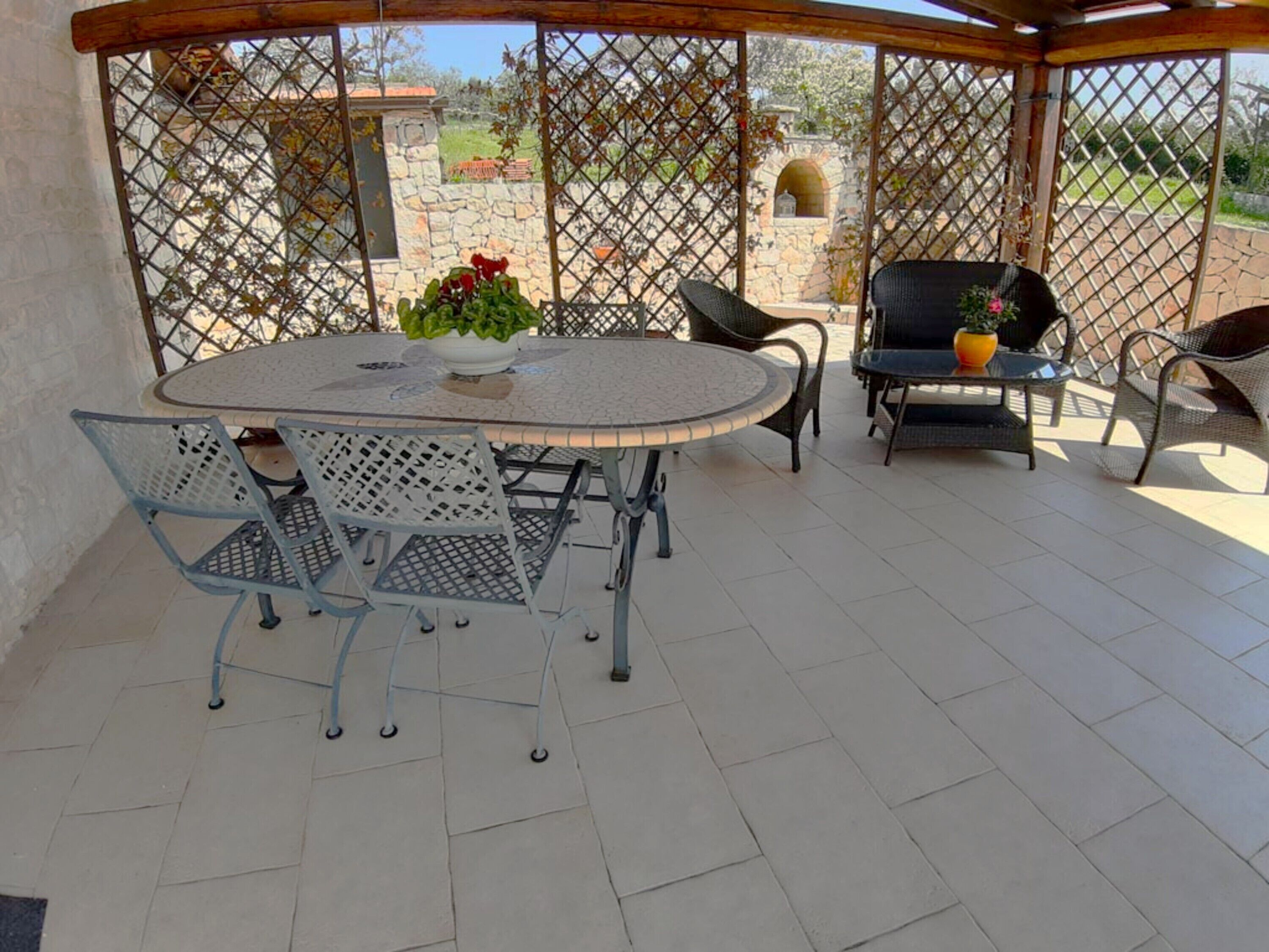 Un patio techado con una mesa redonda y sillas, un muro de piedra, y vistas del paisaje circundante.