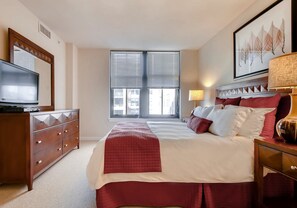 Una habitación de hotel con una cama grande, un aparador, un televisor y una ventana con persianas.
