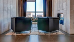 A lobby with two black sofas, a patterned rug, a large window with curtains, and a fireplace. - Bluebird Suites in Pentagon City (Arlington)