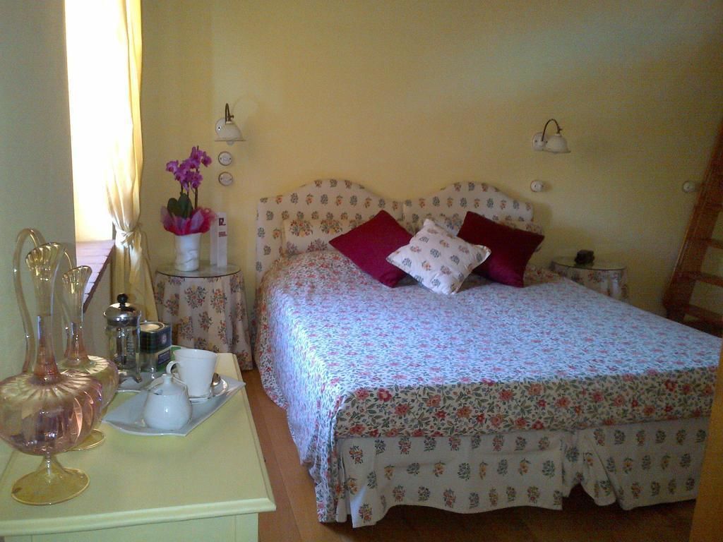 A bedroom with a floral bedspread, two bedside lamps, a bedside table with a vase of flowers, and a small table with a teapot and cups.