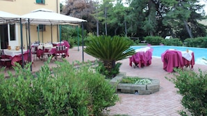 An outdoor patio area with tables and chairs, a pool, and surrounding greenery. - Locanda Strada Della Marina (Senigallia)