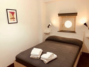 A neatly made bed with two folded towels, a framed artwork on the wall, and a bedside table with a lamp. - Palazzo Rota Guesthouse (Naples)