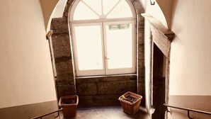 A staircase leading to a room with a large arched window, stone walls, and two potted plants. - Palazzo Rota Guesthouse (Naples)