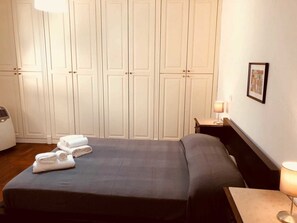 A hotel room with a bed, a desk, a chair, a lamp, and a wardrobe. - Palazzo Rota Guesthouse (Naples)