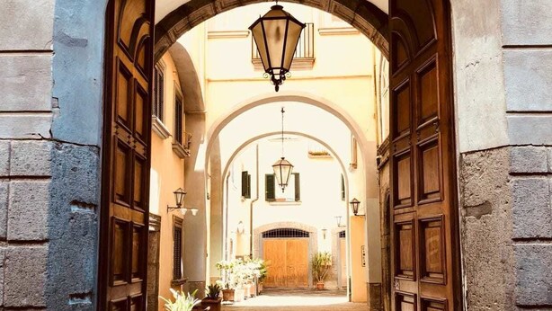 An arched entrance with a wooden door and a hanging lantern, leading into a building with a cobblestone path. - Palazzo Rota Guesthouse (Naples)