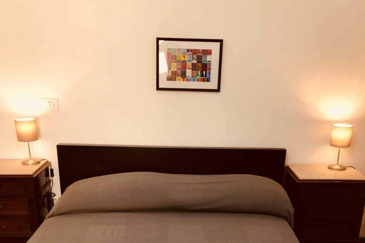 A neatly made bed with two folded white towels at the foot, a dark headboard, and a framed artwork on the wall.