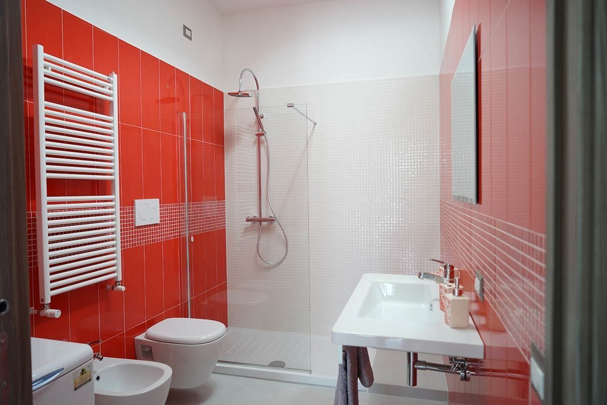 Ein Badezimmer mit roter Fliesenwand, einem weißen Waschbecken und einer Duschkabine.