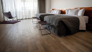 Habitación de hotel con una cama grande, dos mesitas de noche, una silla y vistas a la ciudad a través de cortinas traslúcidas.