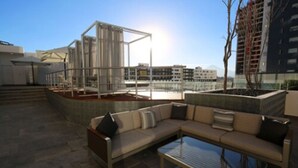 Una terraza en la azotea con un área de estar exterior moderna, que incluye un sofá y una mesa de centro de vidrio.