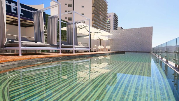 Una piscina con suelo de baldosas, sillas de descanso y sombrillas.
