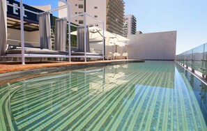 Una piscina con suelo de baldosas, sillas de descanso y sombrillas.