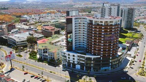 Un hotel moderno con fachada curva, varios balcones y una terraza en la azotea.
