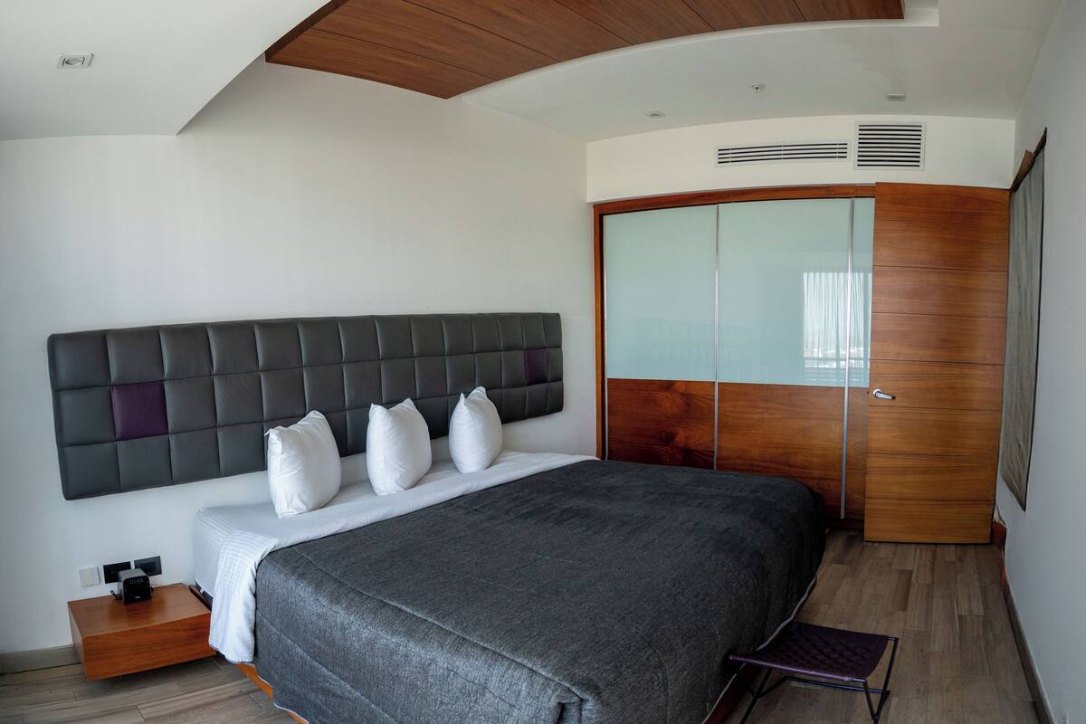 A modern bedroom with a large bed, a wooden wardrobe, and a built-in headboard.
