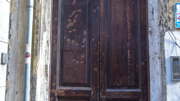 A large, ornate wooden door with a coat of arms above it, set in a weathered building facade. - GuestHouse Marcanto - Duomo (Naples)