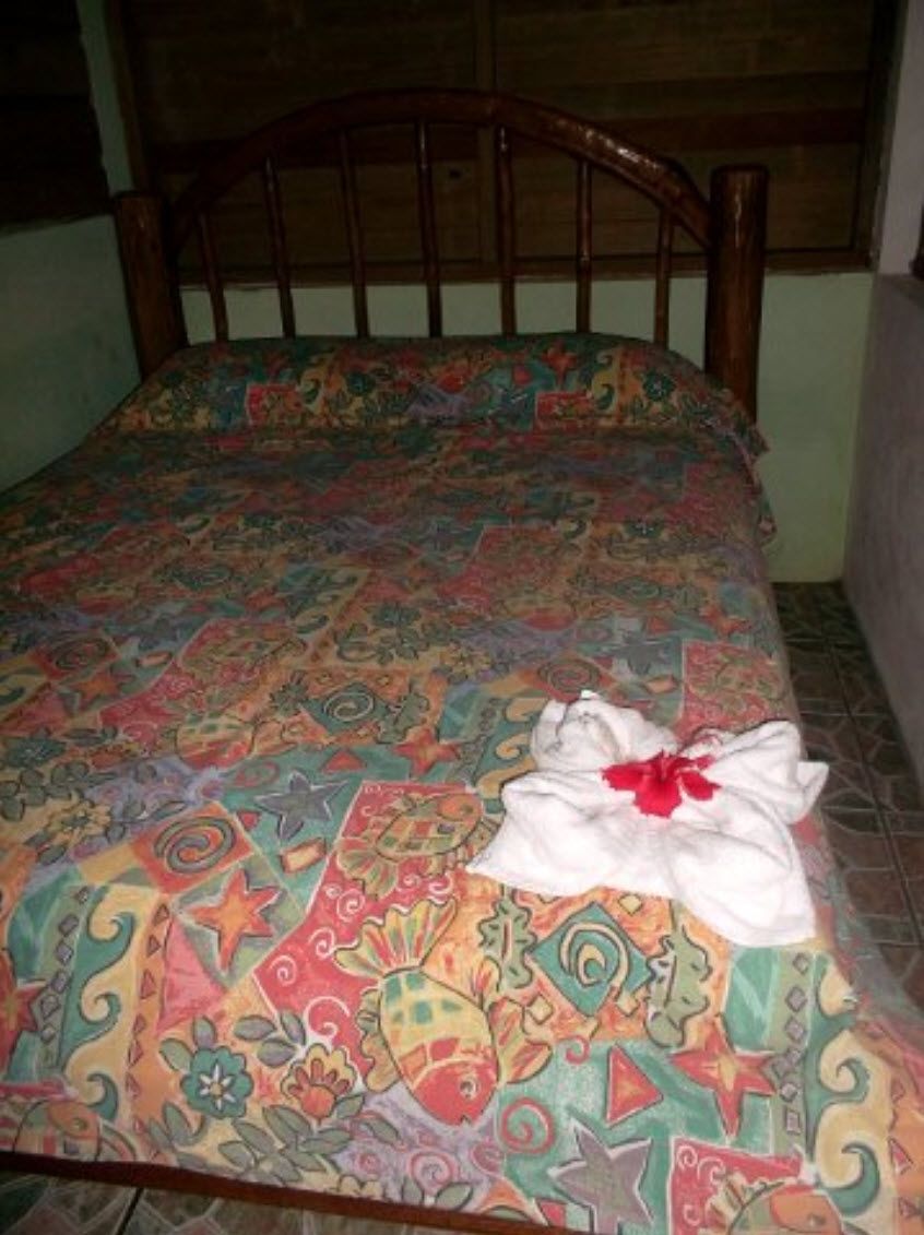 A bed with a patterned bedspread and a white towel with a red flower.