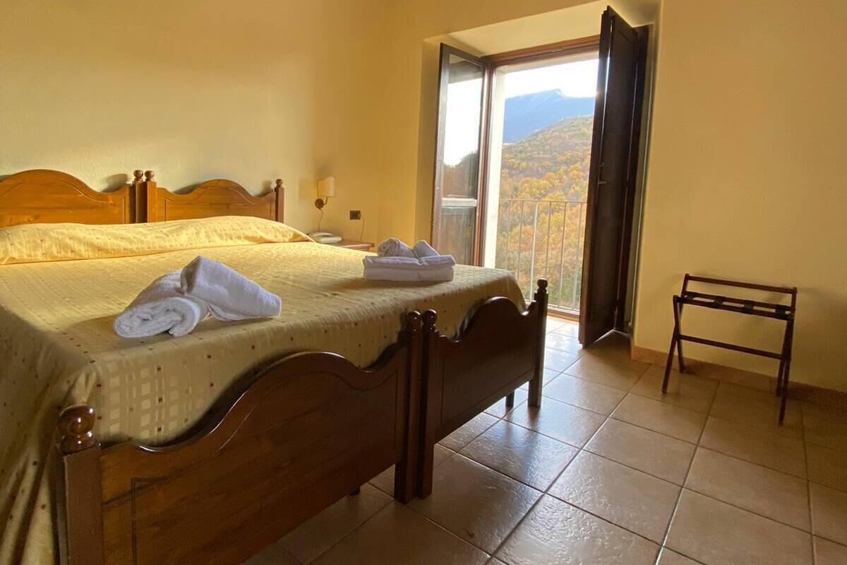A bedroom with a wooden bed, a nightstand, a bedside table, and a view of a mountainous landscape through an open door.