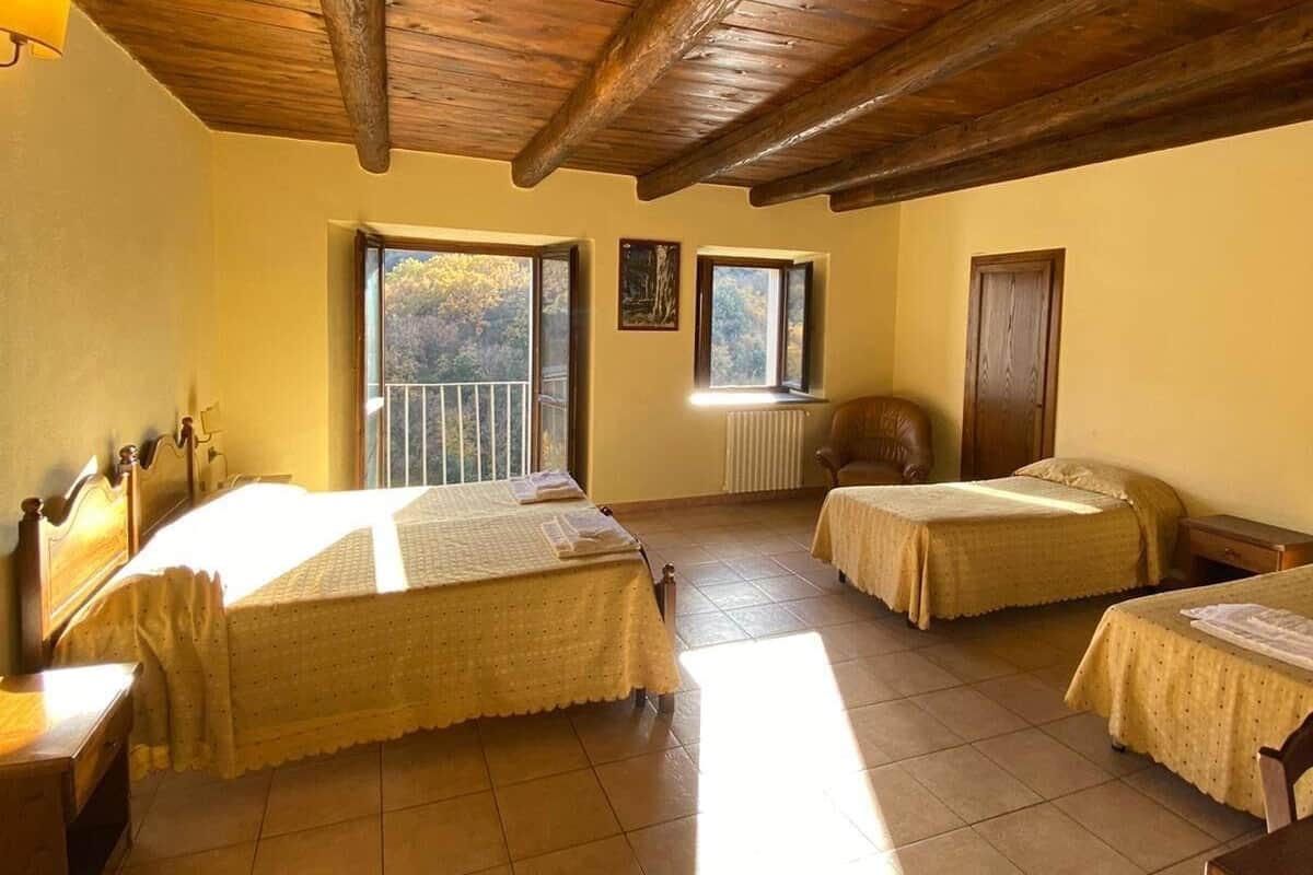 A room with two beds, a wooden ceiling, a window with a view, and a chair.