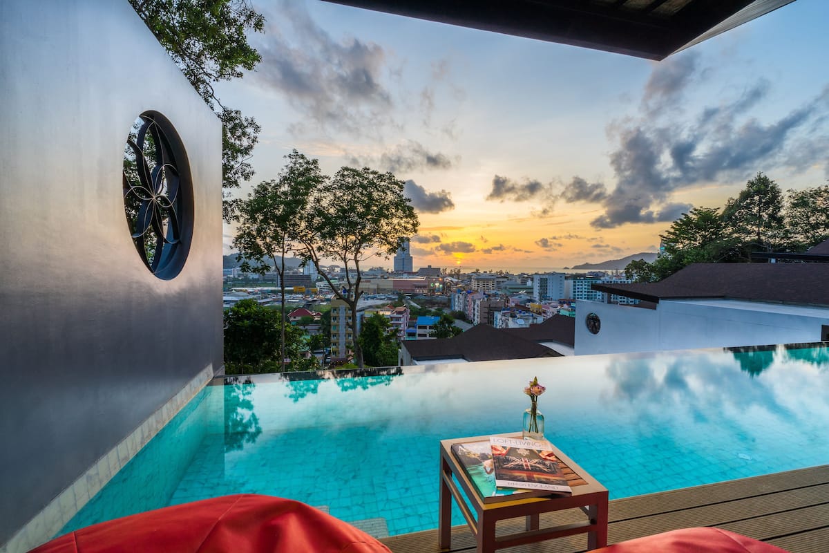 An infinity pool with a city view, a table with a magazine, and a red chair.