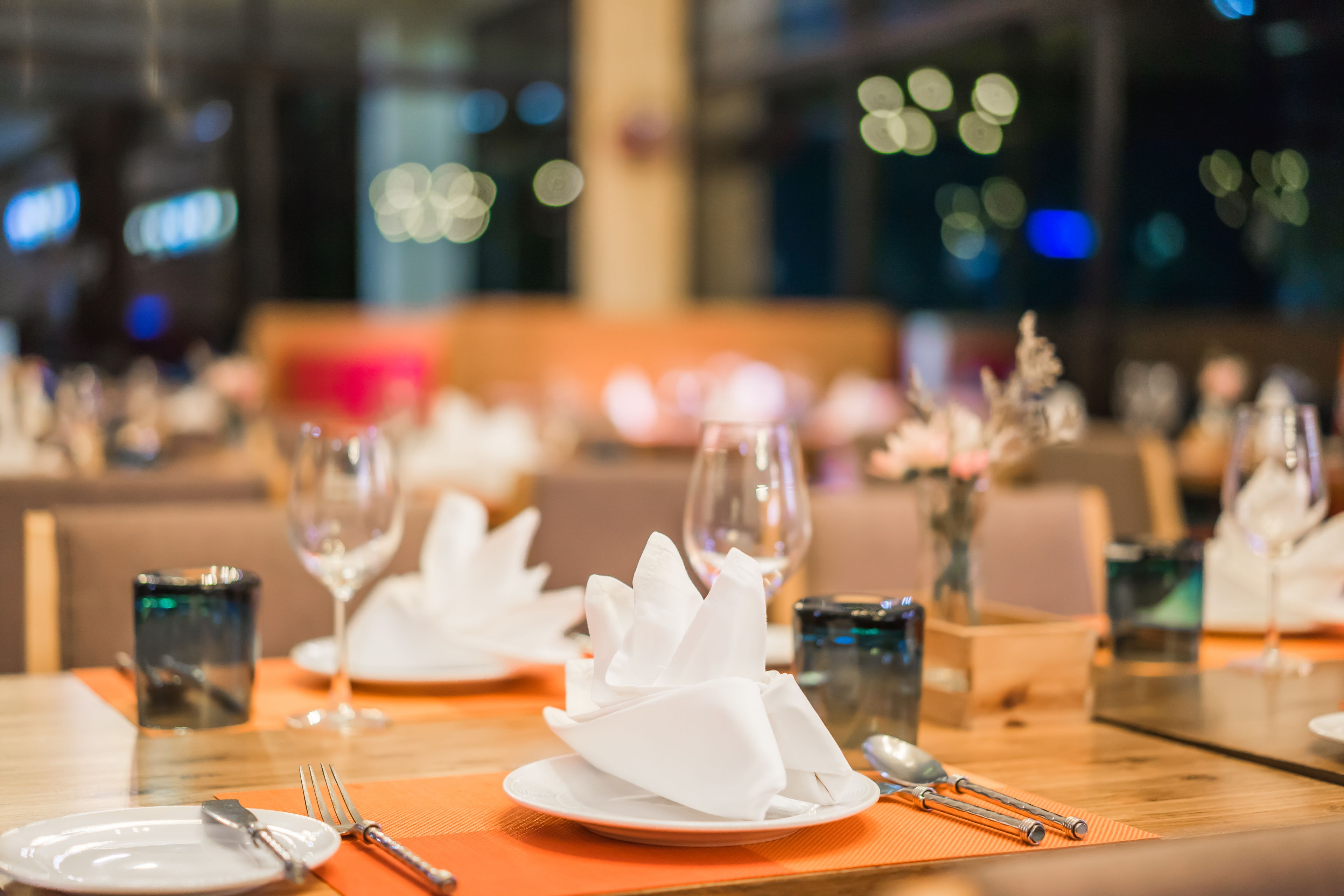 A restaurant setting with tables set for dining, including plates, cutlery, and napkins.