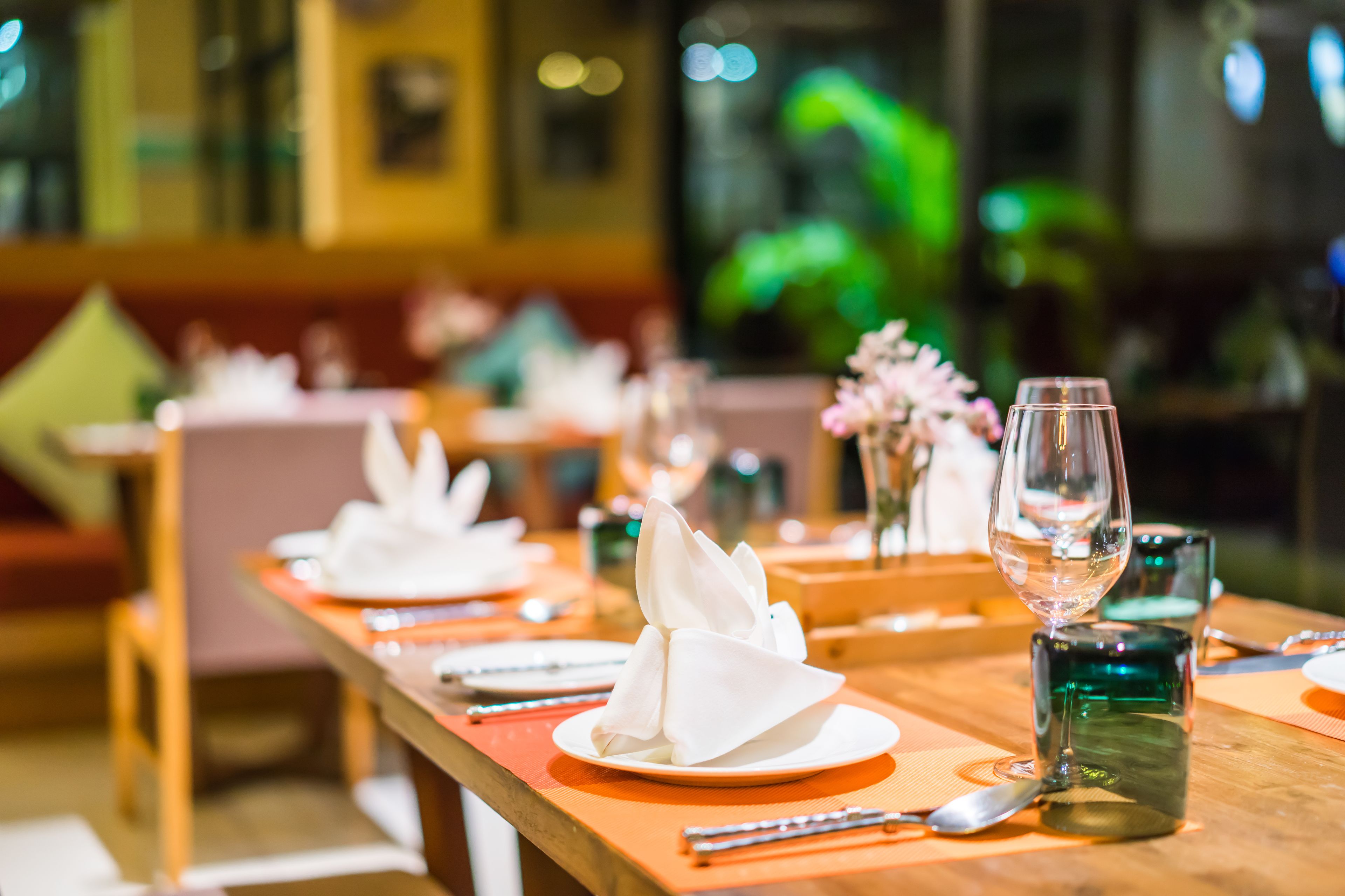 A restaurant setting with neatly arranged tables, each with a folded napkin, a glass of water, and a green glass.