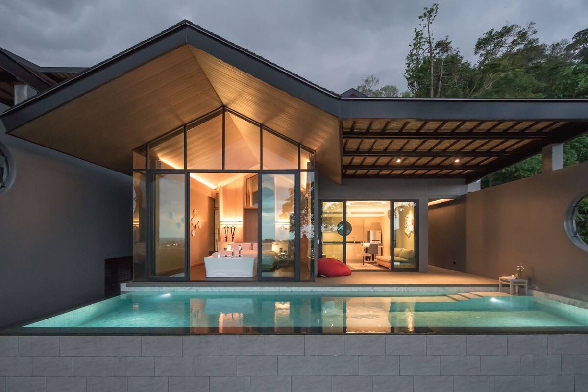 A modern house with a glass-enclosed pool, a covered patio, and a view of the surrounding greenery.