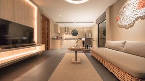 Ein modernes Wohnzimmer mit Flachbildfernseher, einer Couch, einem runden Couchtisch und einer Küche im Hintergrund.