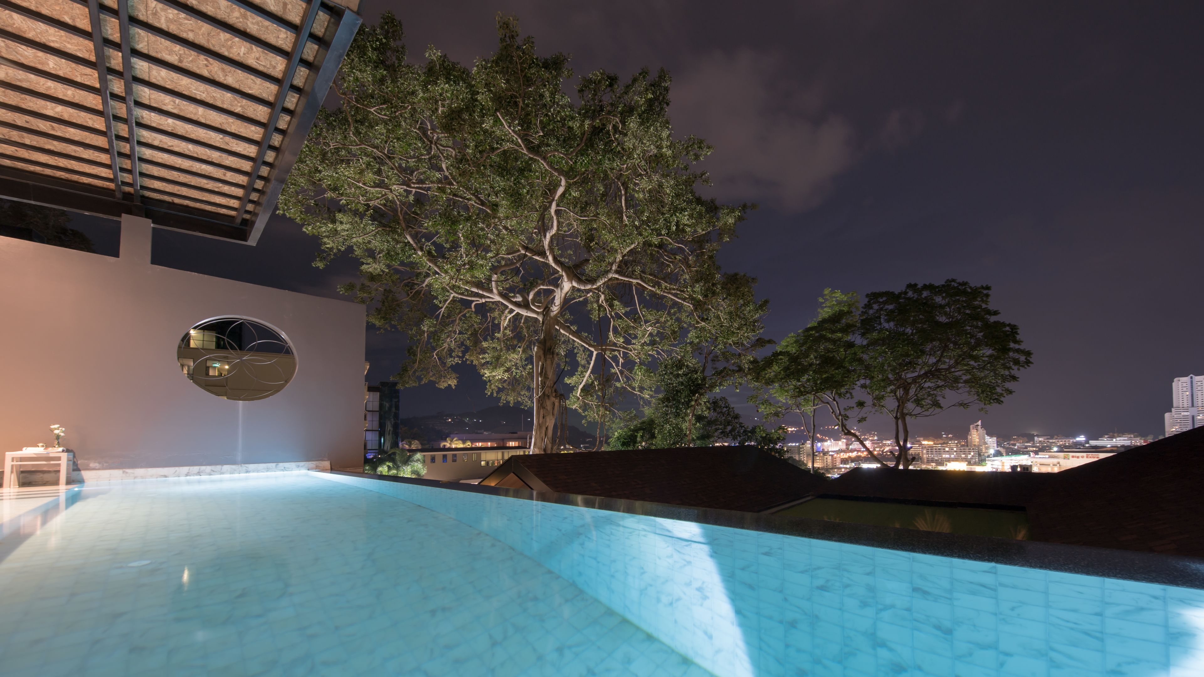 Une piscine extérieure, avec un grand arbre et une vue sur la ville en arrière-plan.