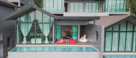 A modern multi-story building with a swimming pool, large windows, and a balcony with outdoor seating.