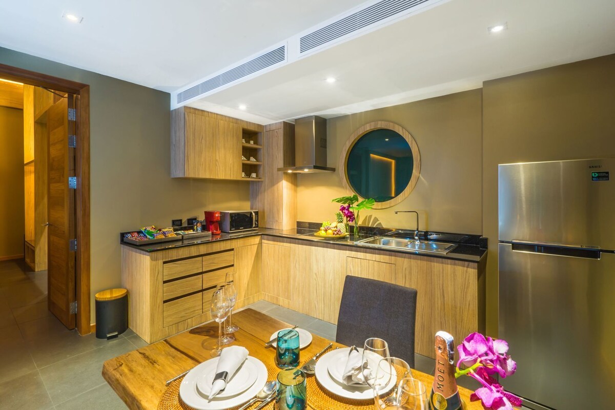 A compact kitchen with wooden cabinets, a built-in microwave, a stainless steel refrigerator, and a dining area with a table set for two.