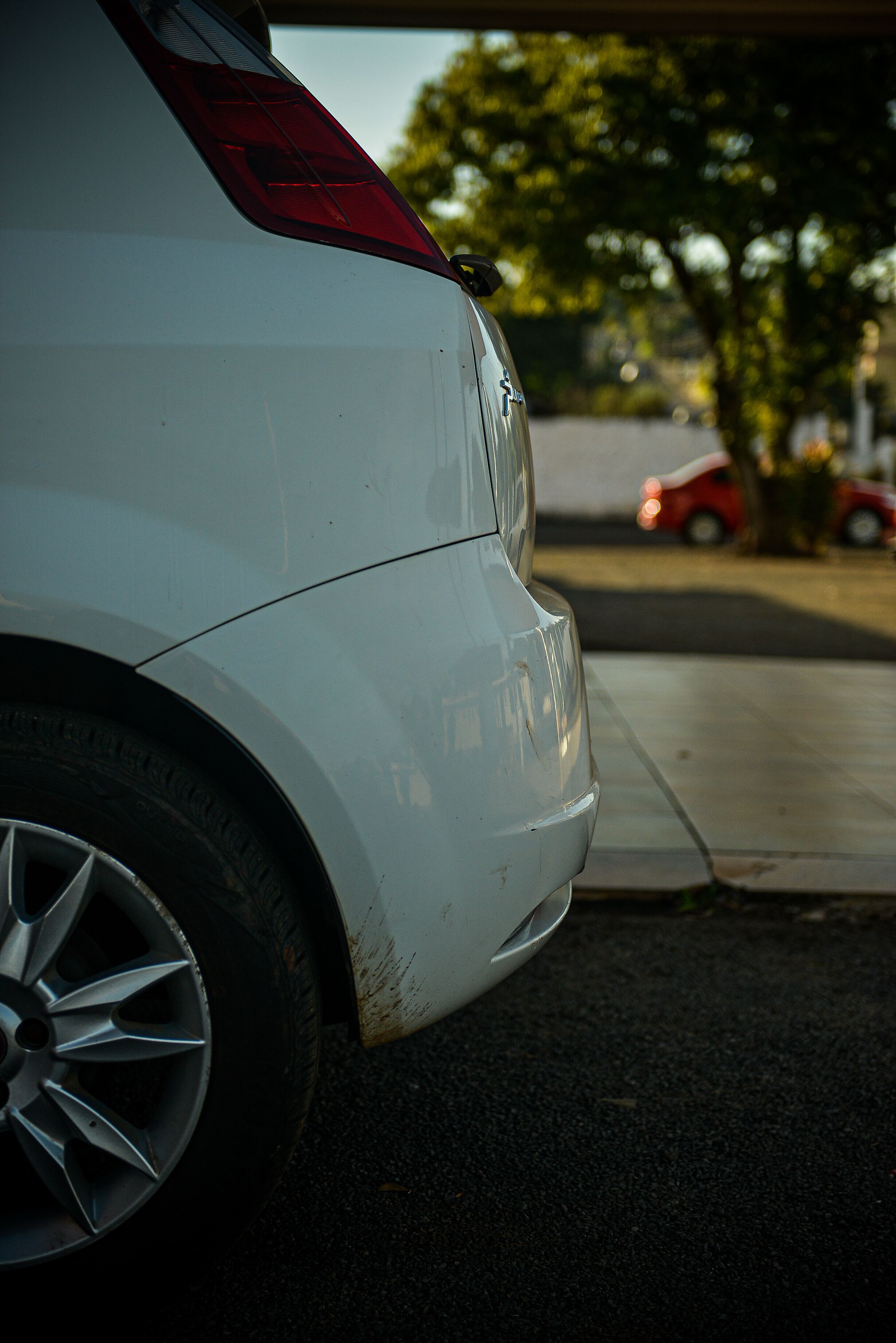 A white car parked on a street with a visible rear tire and part of the car's body.