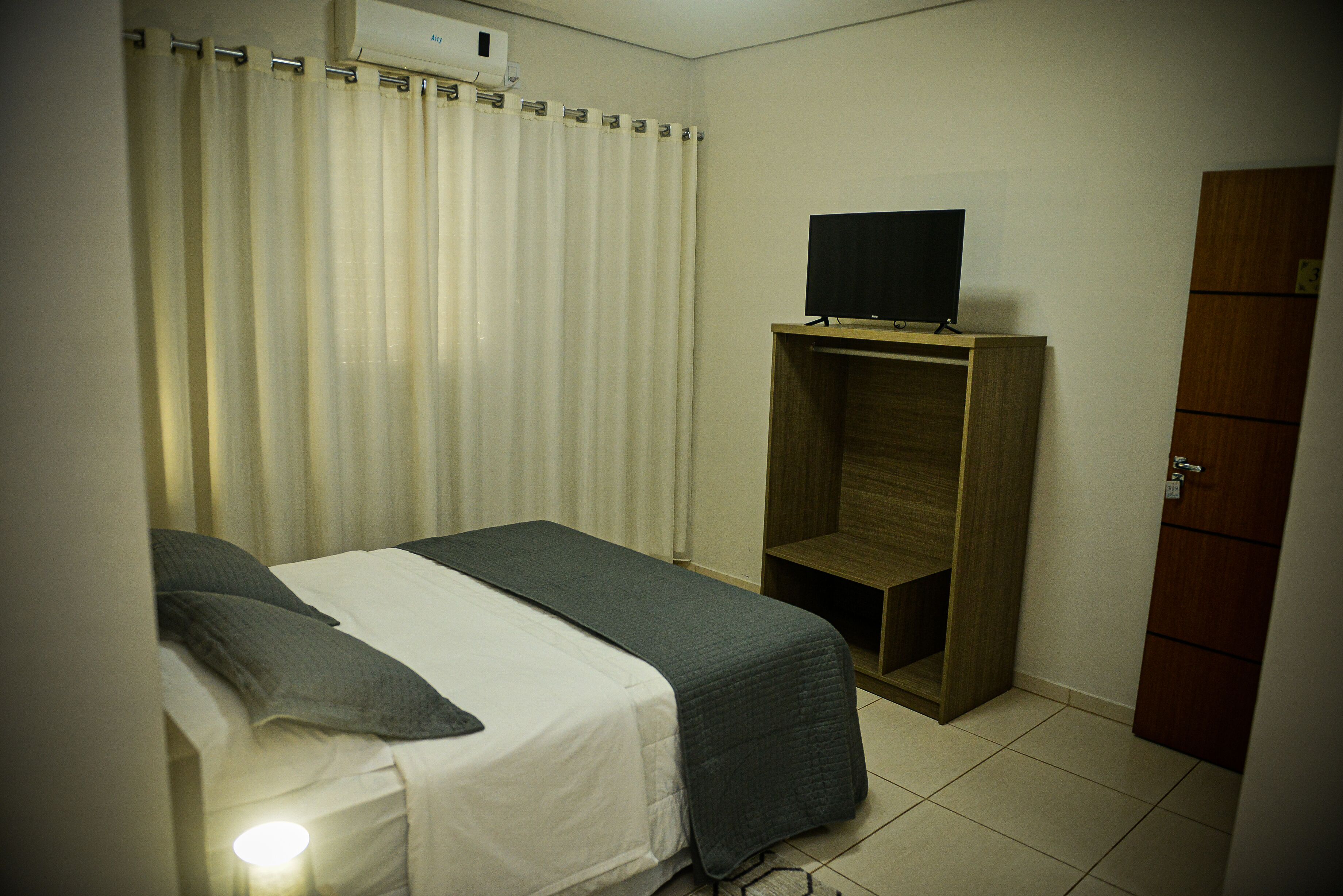A hotel room with a bed, a TV on a wooden stand, a wardrobe, and a curtain.