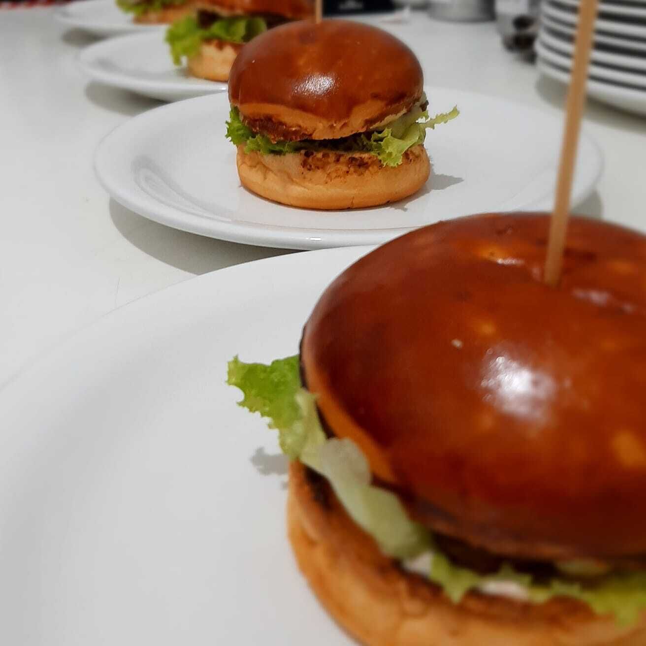Uma mesa com pratos brancos, cada um com um hambúrguer e um palito.