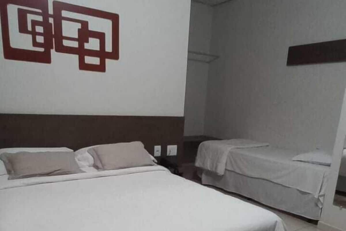 Ein Hotelzimmer mit einem großen Bett, einem kleineren Bett und einem an der Wand befestigten Regal.