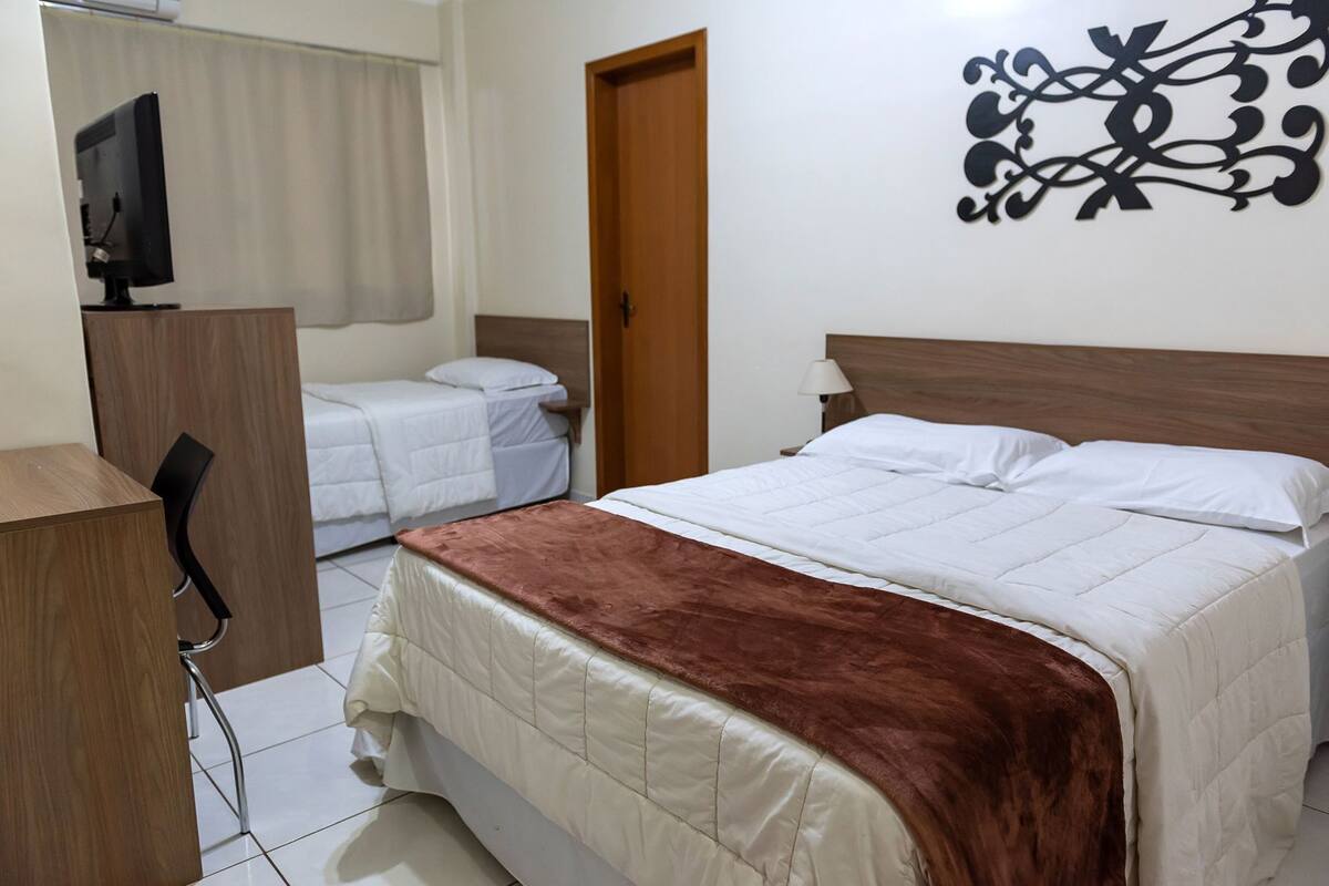 Ein Schlafzimmer mit Bett, Schreibtisch, Stuhl, Fernseher und einer Tür.
