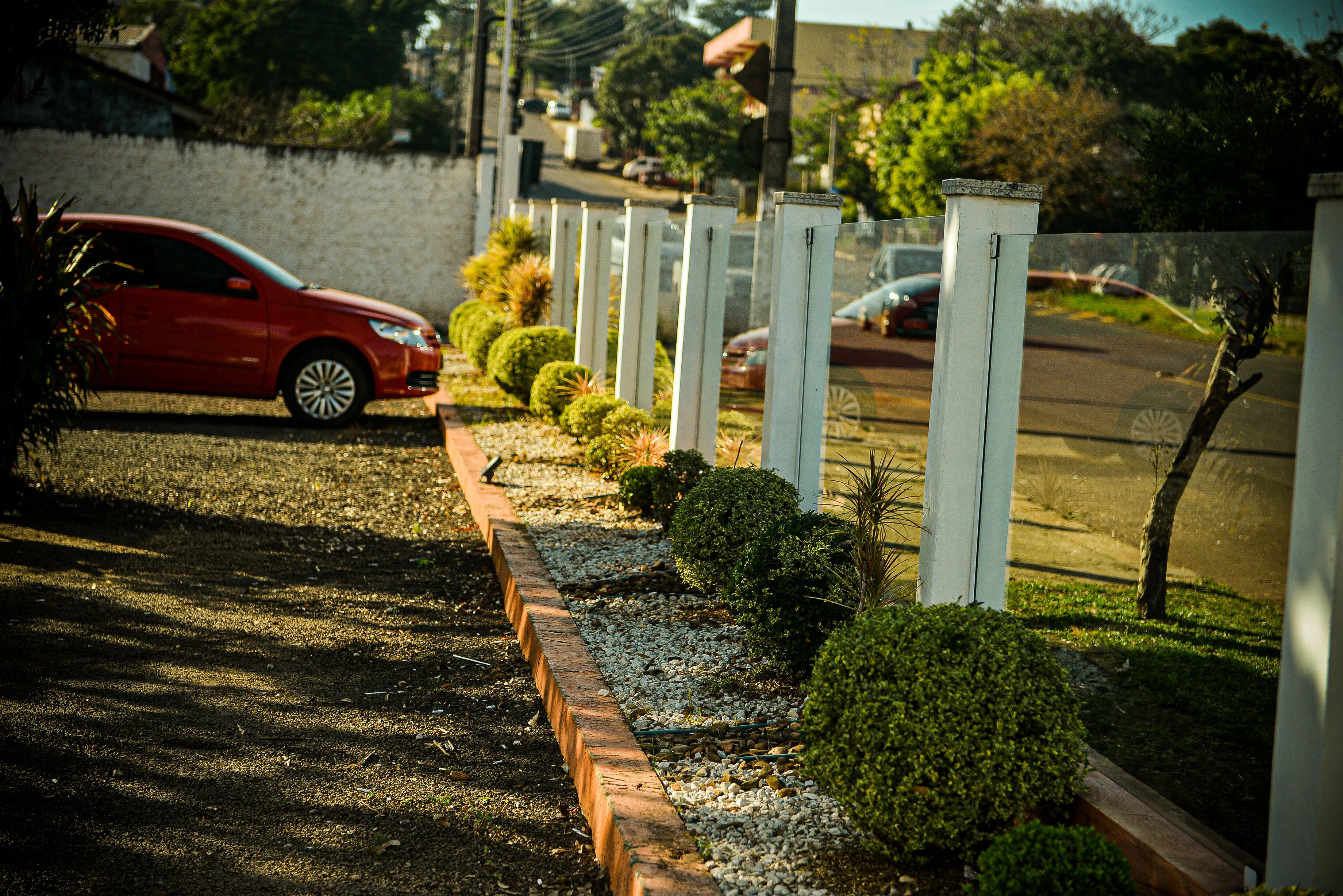 A red car parked on a gravel driveway with a row of white bollards and neatly trimmed bushes.