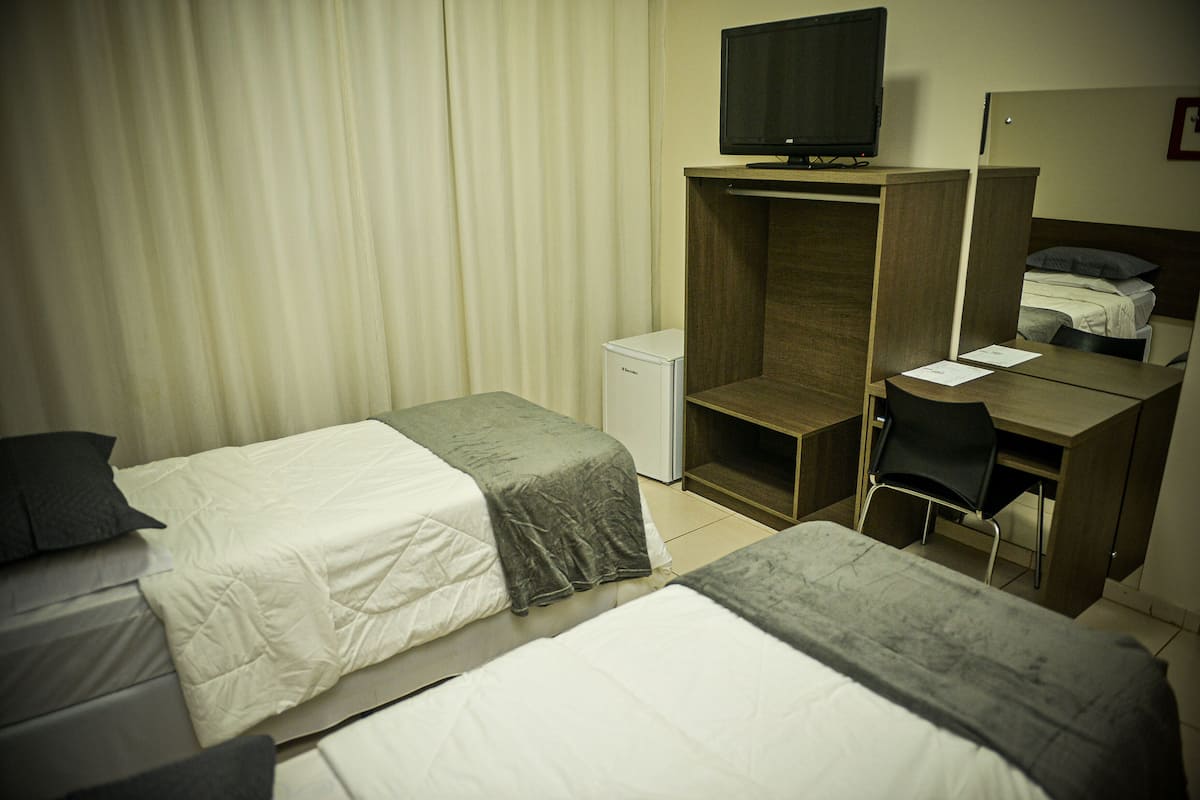 Ein Hotelzimmer mit zwei Betten, einem Schreibtisch, einem Stuhl, einem Fernseher und einem kleinen Kühlschrank.