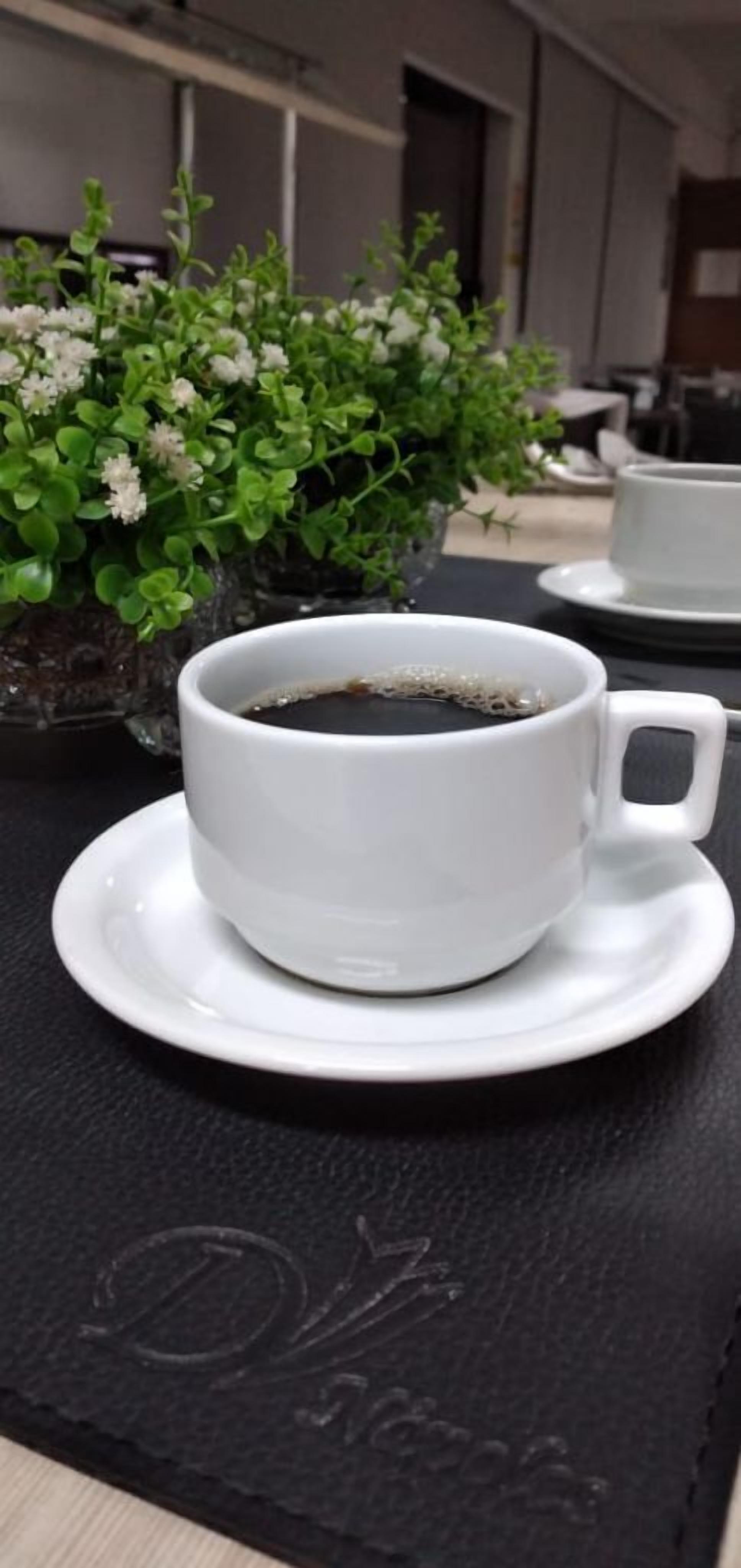 A white cup of coffee on a saucer, placed on a table with a black placemat.