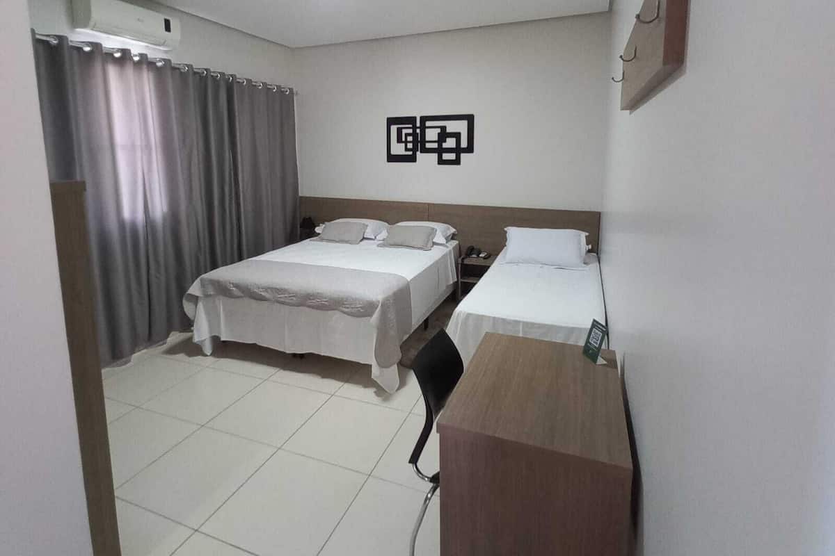 Ein Hotelzimmer mit zwei Betten, einem Schreibtisch, einem Stuhl, einer Wandlampe und einem Vorhang.